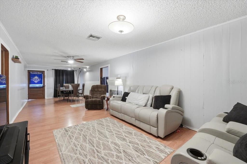 A living room with light wood flooring, a white sofa, and a dining area beyond — 675 E BAY AVENUE, EAGLE LAKE, FL