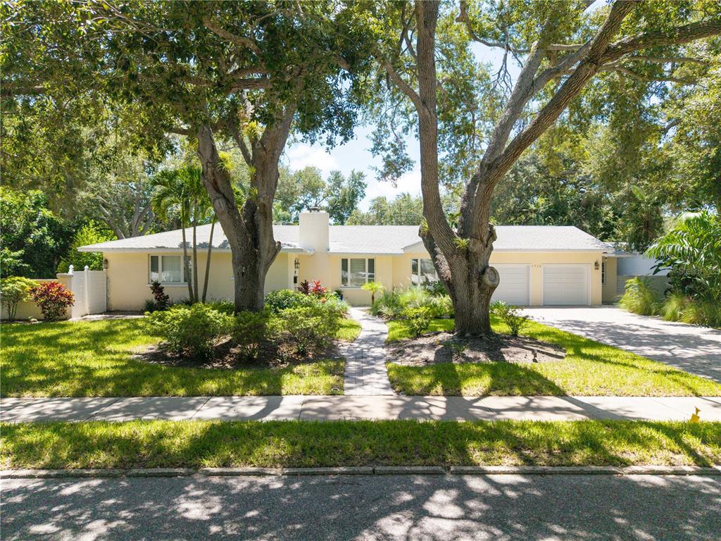 A single-story house with a light yellow exterior, a two-car garage, and large oak trees — 1722 NORTH DRIVE, SARASOTA, FL