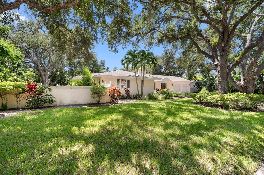 A single-story house with a light-colored exterior, a low wall, and mature trees in front — 1722 NORTH DRIVE, SARASOTA, FL