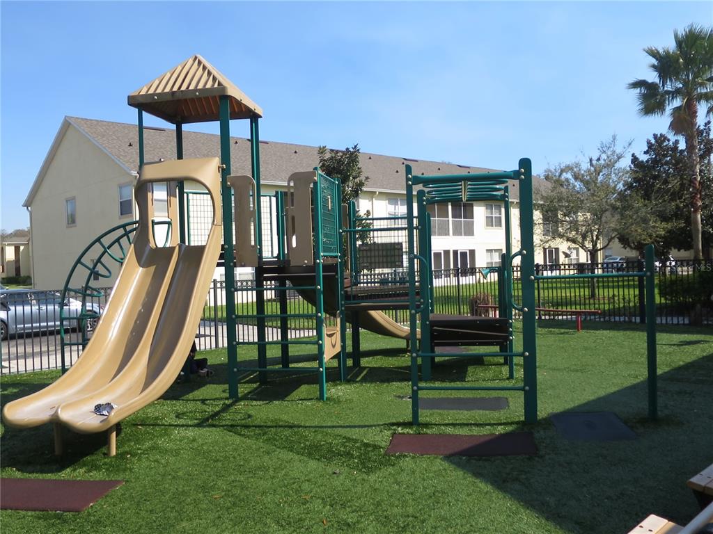 A playground with a double slide and climbing structure sits on a grassy area — 2806 CLUB CORTILE CIRCLE UNIT B, KISSIMMEE, FL