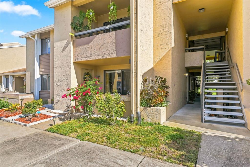 An exterior view of a two-story apartment building with a staircase and a small garden — 5195 VINELAND ROAD UNIT B102, ORLANDO, FL