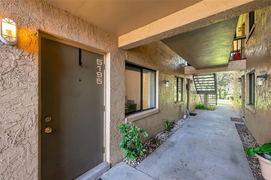 An exterior view of a ground-level apartment entrance with a brown door and concrete walkway — 5195 VINELAND ROAD UNIT B102, ORLANDO, FL