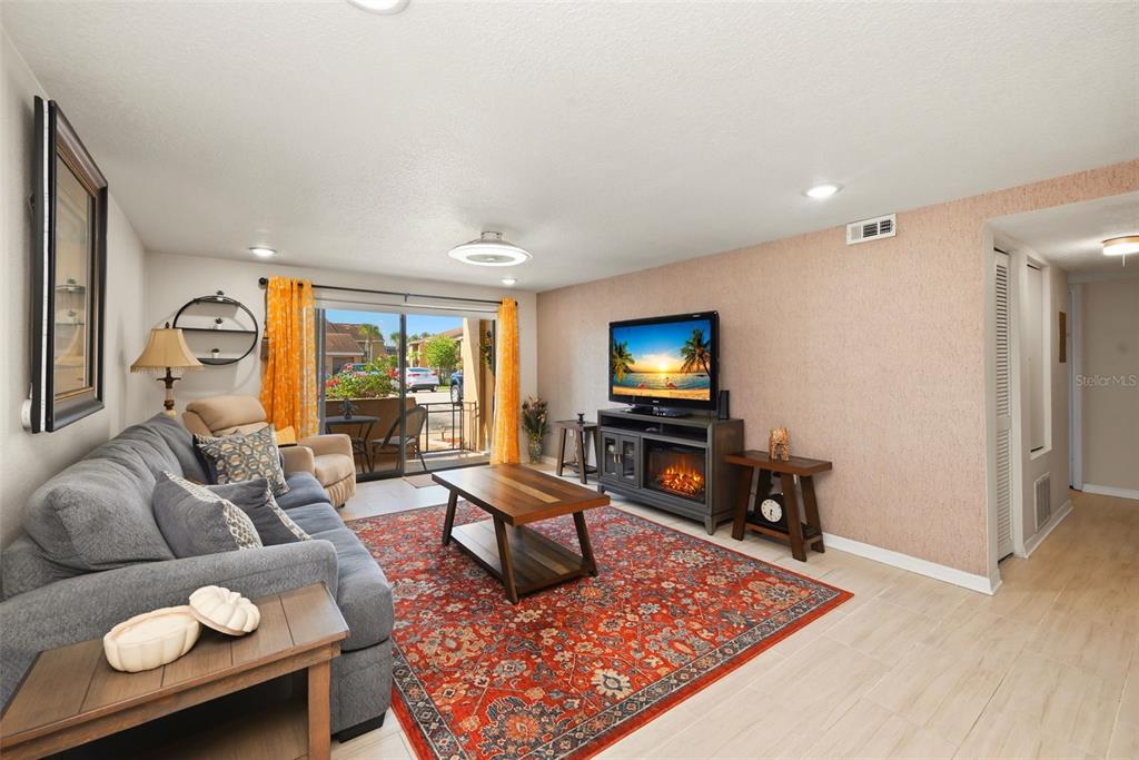 A living room features a gray sofa, a patterned red rug, and a television stand — 5195 VINELAND ROAD UNIT B102, ORLANDO, FL