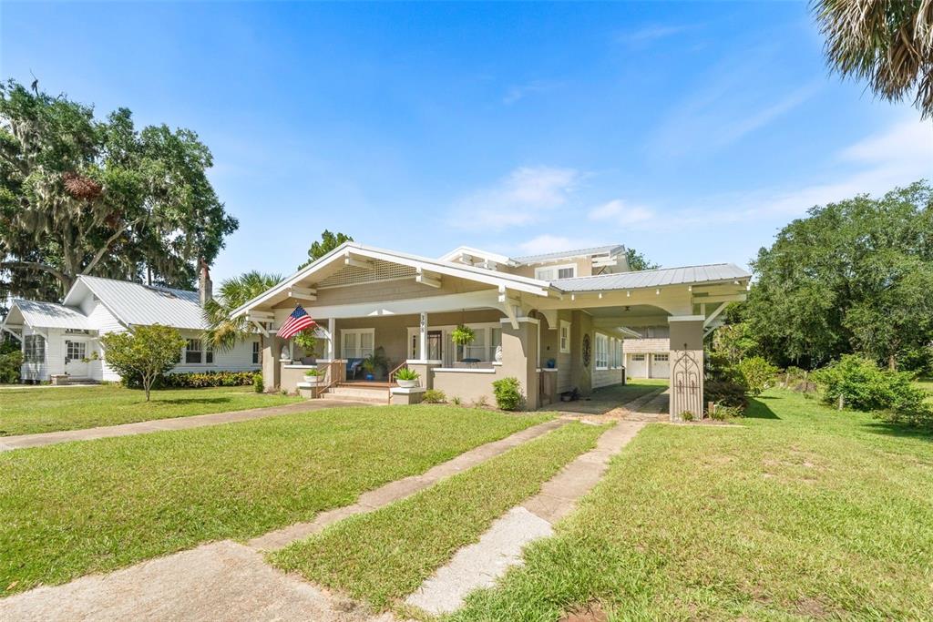 A tan bungalow with a front porch, metal roof, and a side carport on grass — 398 S MARION AVENUE, LAKE CITY, FL