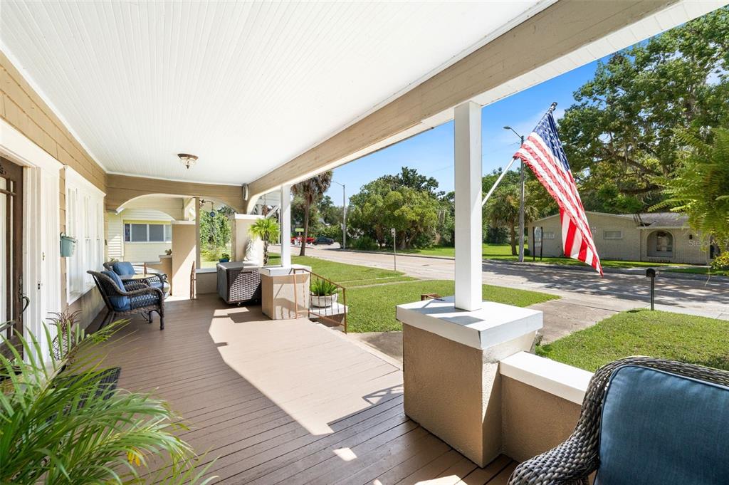 A covered wooden porch features white columns, wicker furniture, and an American flag on display — 398 S MARION AVENUE, LAKE CITY, FL