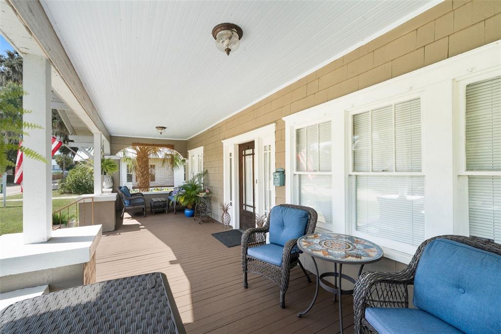 A covered wooden porch features wicker chairs, a small table, and white trim — 398 S MARION AVENUE, LAKE CITY, FL