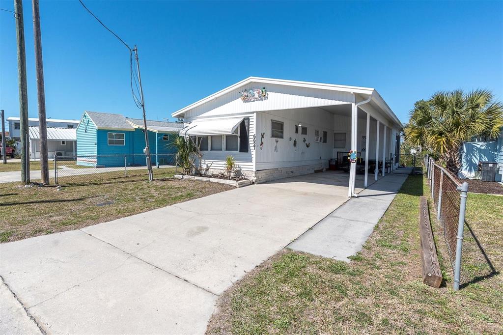 A white mobile home features a concrete driveway, a carport, and a chain-link fence — 6627 TOWER DRIVE, HUDSON, FL