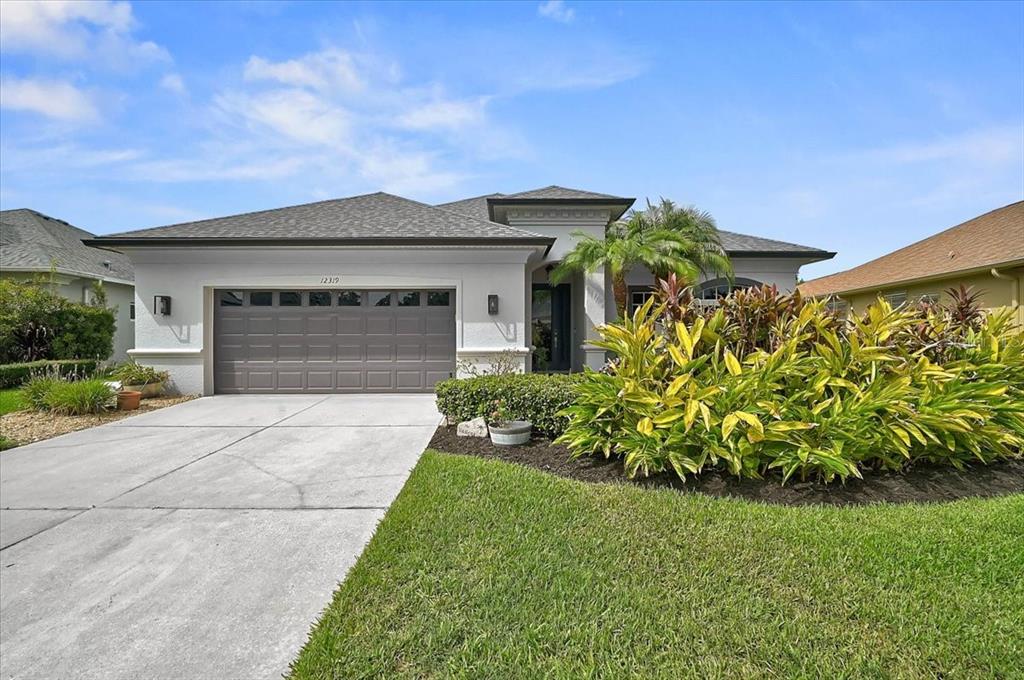 A single-story house with a gray garage door, white stucco exterior, and landscaped front yard — 12319 LAVENDER LOOP, BRADENTON, FL