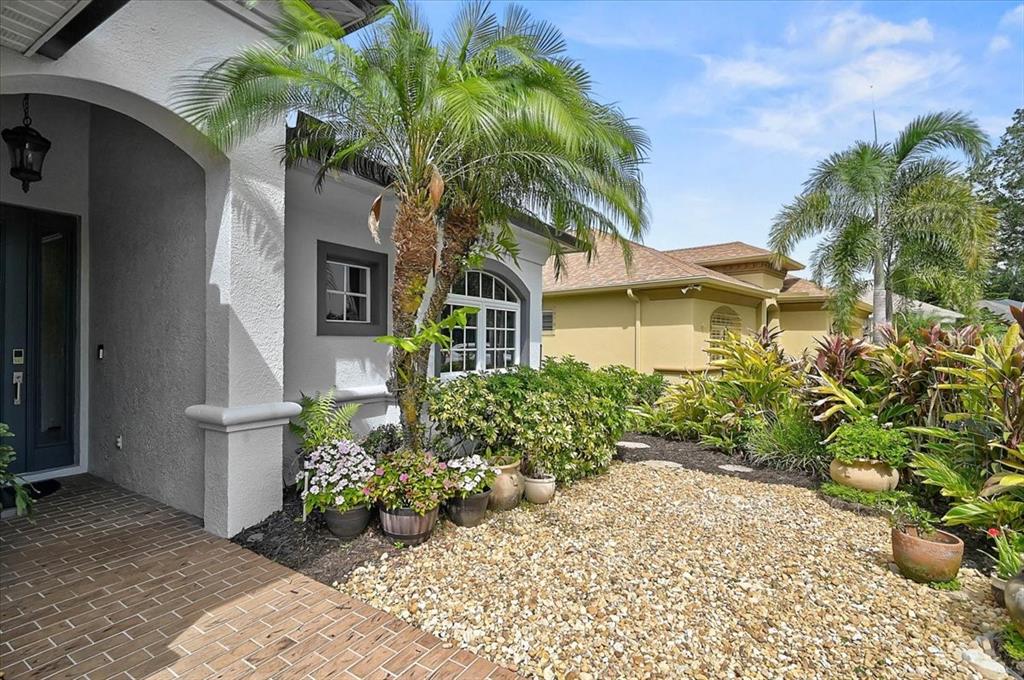 A front entryway features a brick porch, a palm tree, and a gravel garden bed — 12319 LAVENDER LOOP, BRADENTON, FL