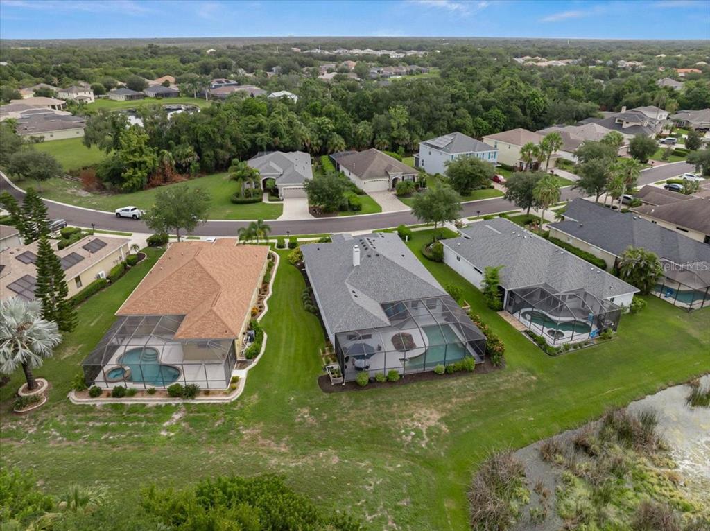 An aerial view shows three suburban houses with screened-in pools overlooking a grassy pond area — 12319 LAVENDER LOOP, BRADENTON, FL