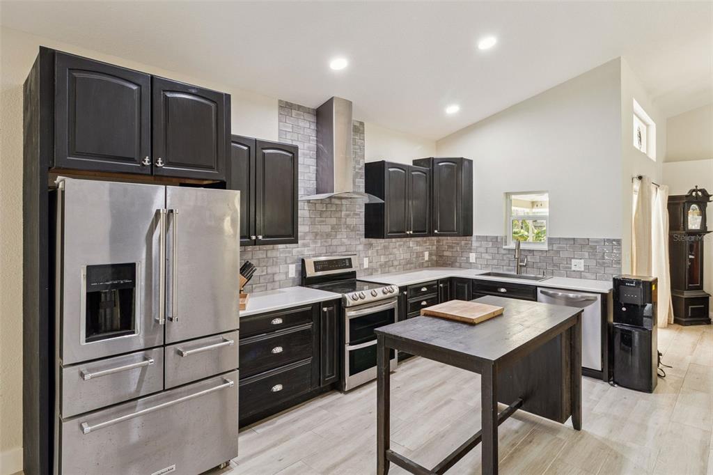A kitchen features dark wood cabinets, stainless steel appliances, gray subway tile, and a wooden island — 105 TRADEWINDS TER, INDIALANTIC, FL