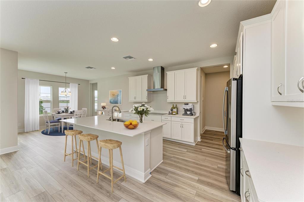 A modern kitchen features white cabinetry, a large island with bar stools, and wood-look flooring — 10186 SURREY ROSE DRIVE, SAN ANTONIO, FL