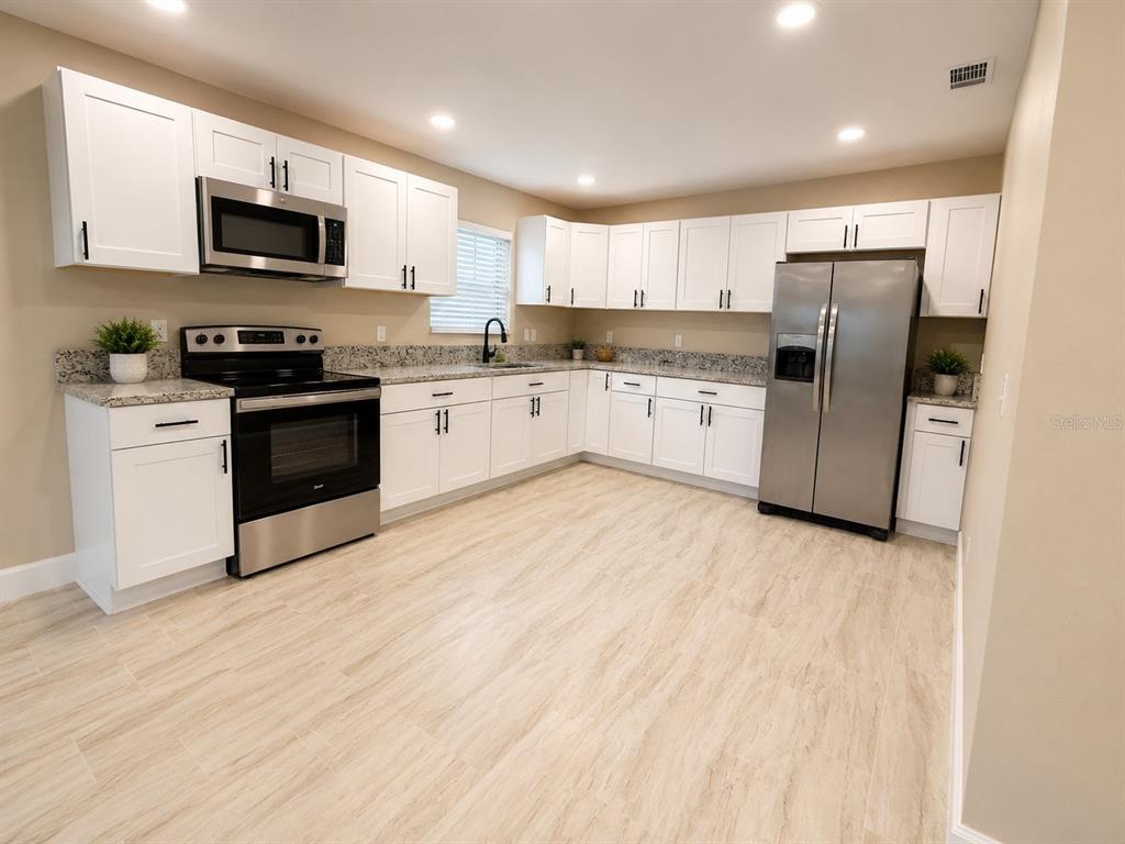 A kitchen features white cabinets, stainless steel appliances, granite countertops, and light-colored wood-look flooring — 2103 45TH STREET COURT E, BRADENTON, FL