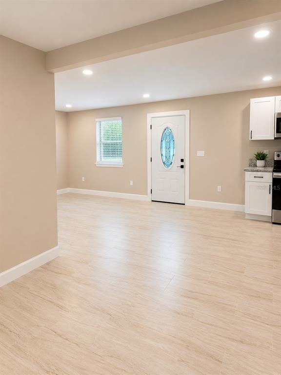 An open-concept room features light-colored wood-look flooring, beige walls, and a white front door — 2103 45TH STREET COURT E, BRADENTON, FL