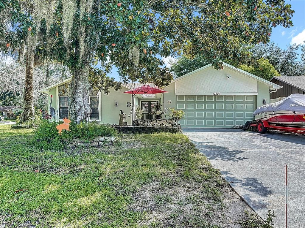 A single-story house with a green garage, a large tree, and a boat in the driveway — 12529 SHADOW RIDGE BOULEVARD, HUDSON, FL