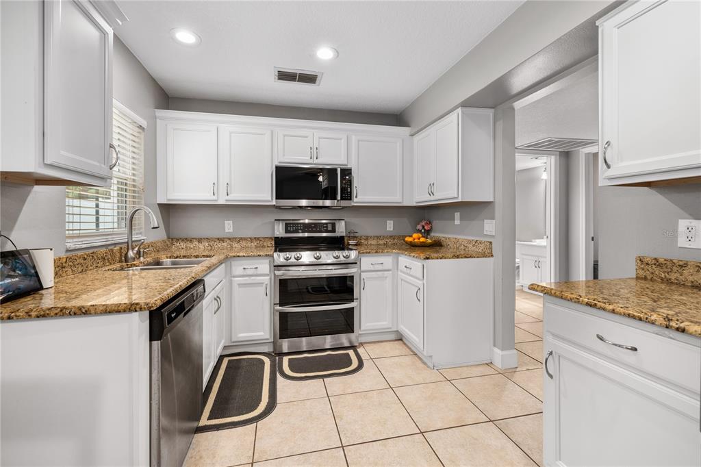 A kitchen with white cabinets, granite countertops, stainless steel appliances, and beige tile flooring — 1154 DEER LAKE CIRCLE, APOPKA, FL