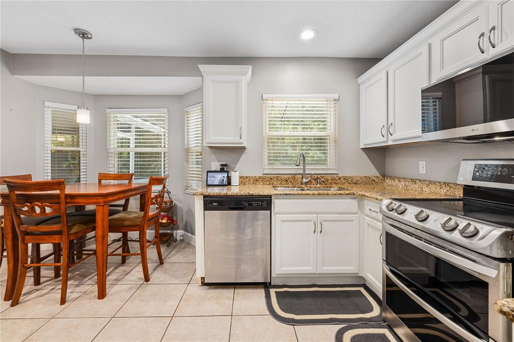 A kitchen features white cabinets, granite countertops, stainless steel appliances, and an adjacent dining area — 1154 DEER LAKE CIRCLE, APOPKA, FL