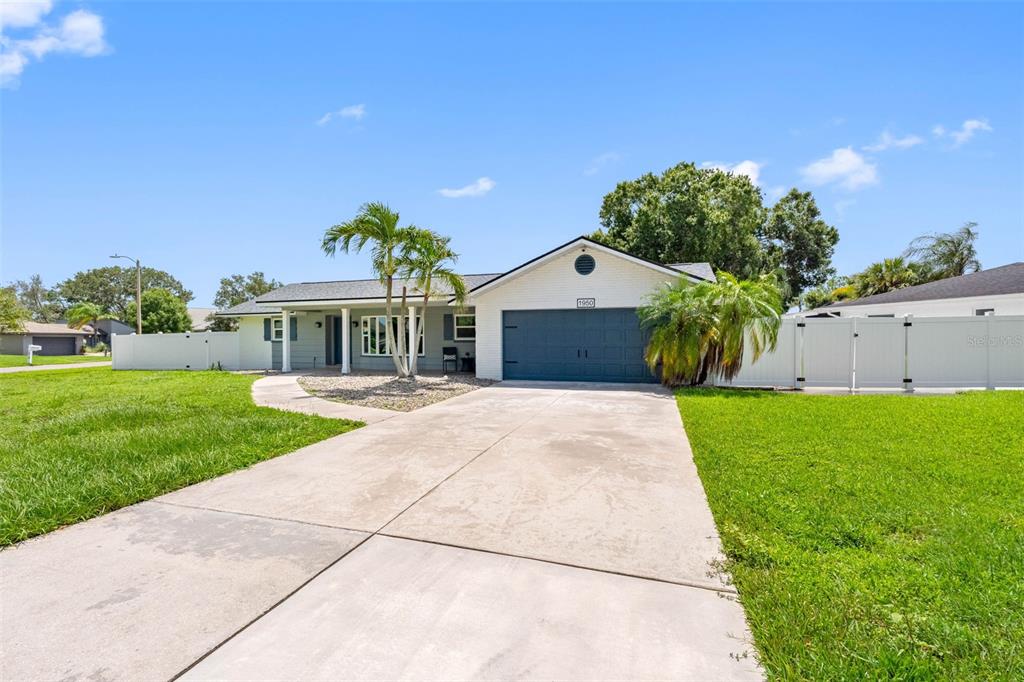 A single-story house with a white brick exterior, a dark garage door, and palm trees — 1950 ARVIS CIRCLE W, CLEARWATER, FL