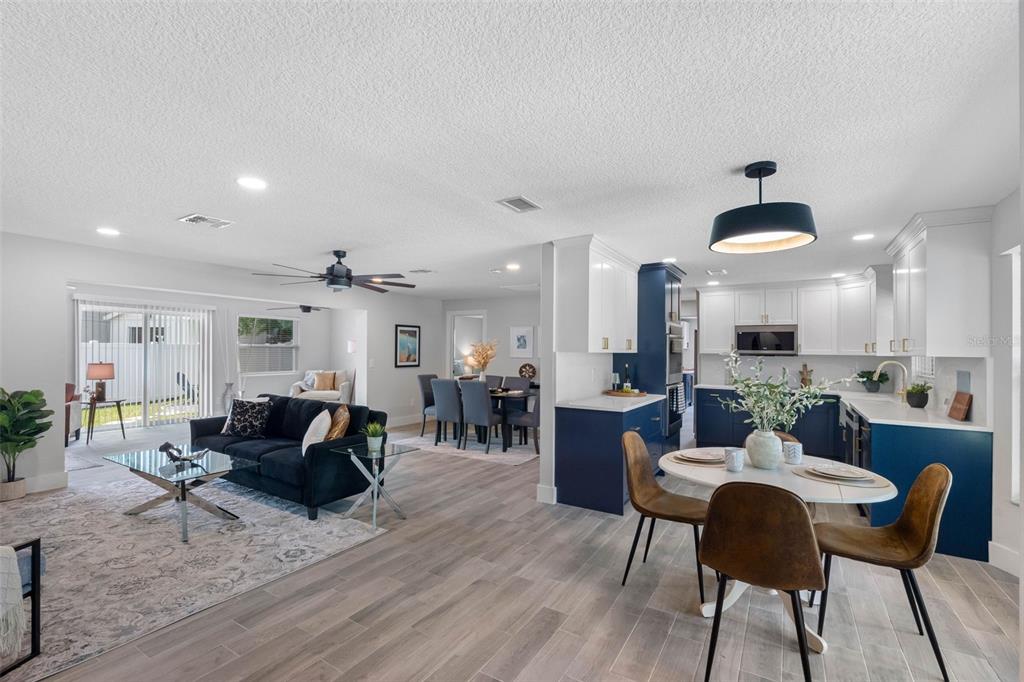 An open-concept living and dining area features a kitchen with blue cabinetry and wood flooring — 1950 ARVIS CIRCLE W, CLEARWATER, FL