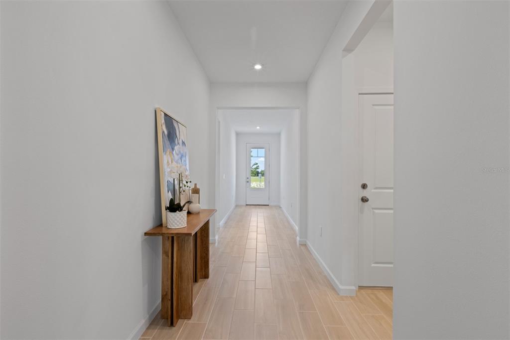 A long, light-filled hallway features wood-look tile flooring, white walls, and a wooden console table — 2600 GINSENG IVY STREET, APOPKA, FL