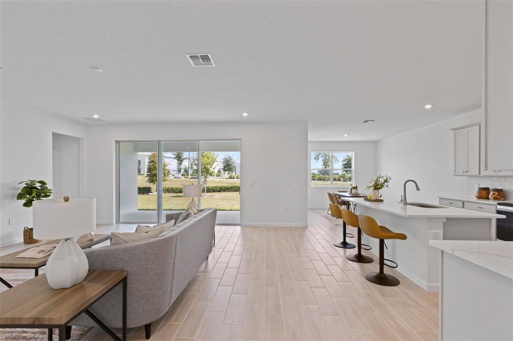 An open-concept living room and kitchen featuring light wood-look tile floors and sliding glass doors — 2600 GINSENG IVY STREET, APOPKA, FL