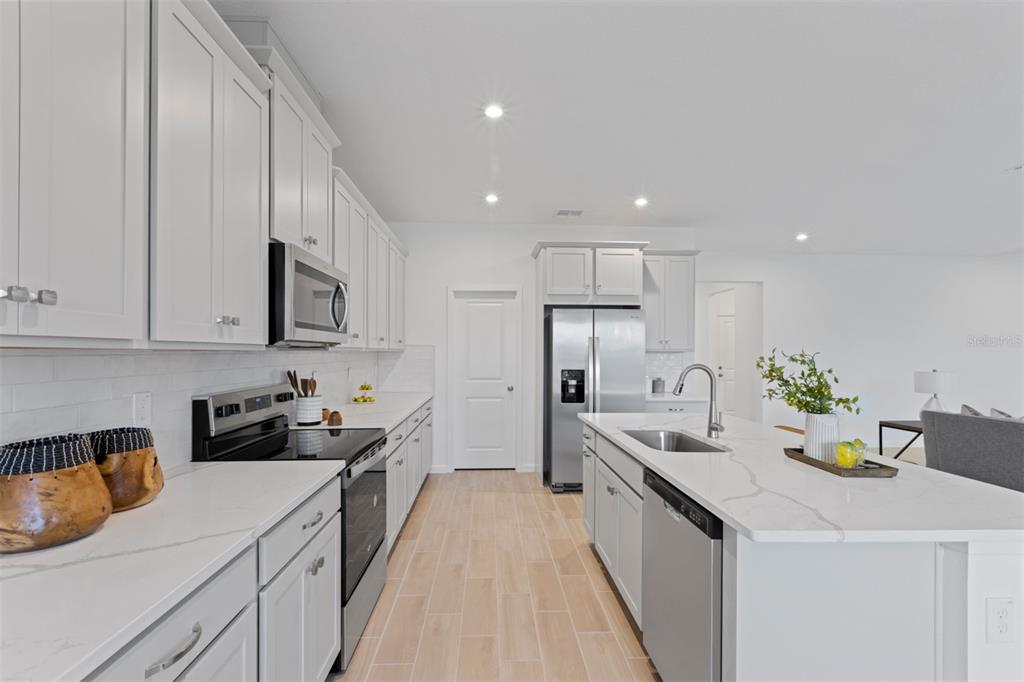 A modern kitchen features white cabinets, stainless steel appliances, and a quartz-topped center island — 2600 GINSENG IVY STREET, APOPKA, FL