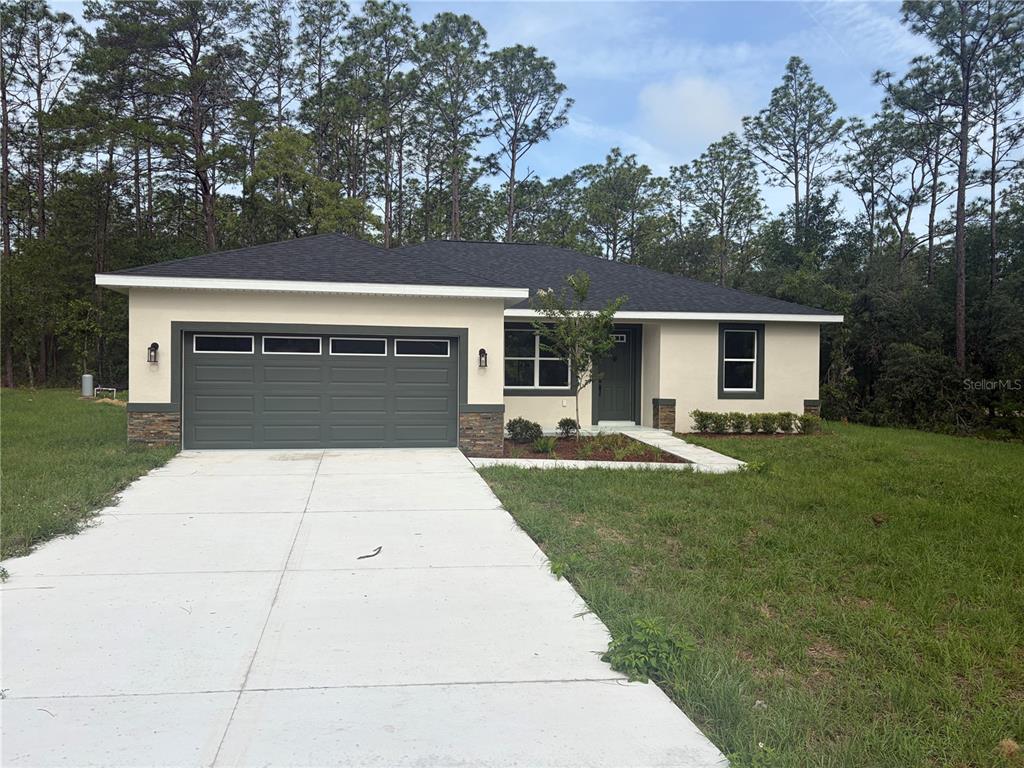 A single-story house with a green garage door, white stucco walls, and stone accents — 6860 SW 135TH TERRACE ROAD, OCALA, FL