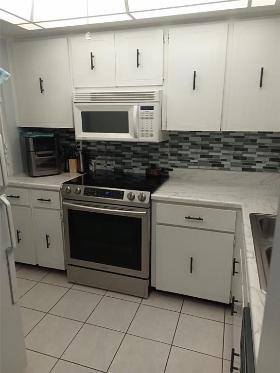 A kitchen features white cabinets, stainless steel appliances, a tiled backsplash, and light-colored countertops — 3354 SCORECARD DRIVE, NEW PORT RICHEY, FL