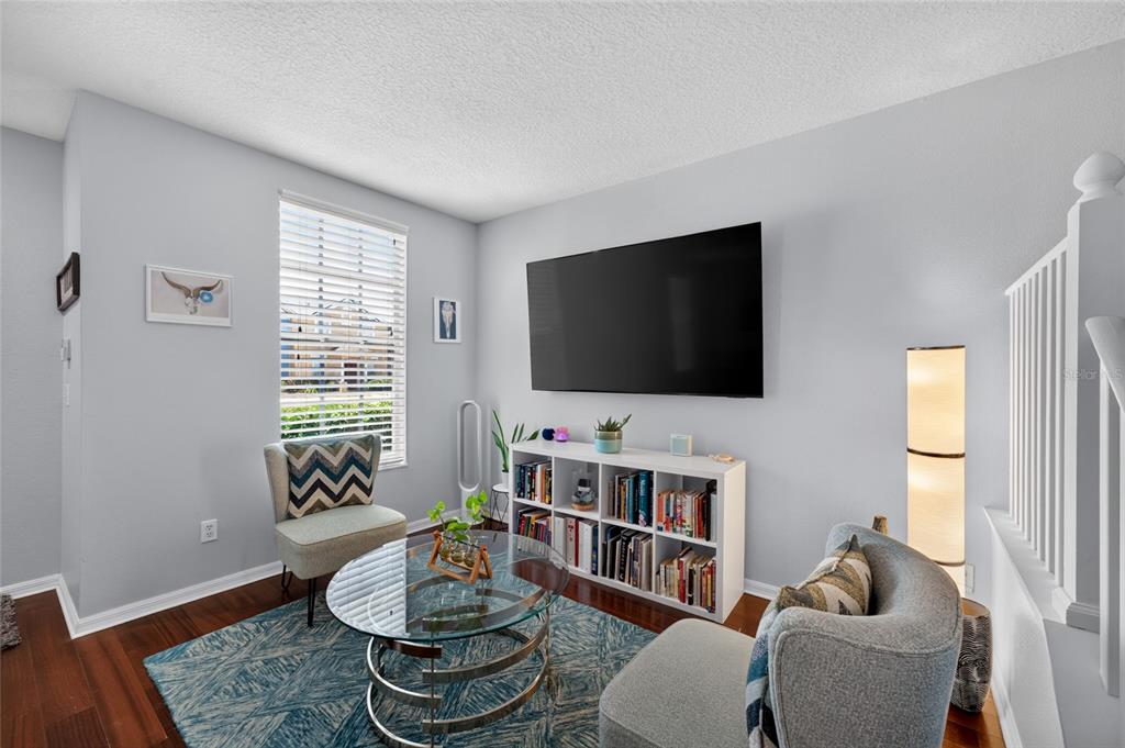 A living room features a television, a white bookshelf, two armchairs, and a glass coffee table — 30211 SWINFORD LANE, WESLEY CHAPEL, FL