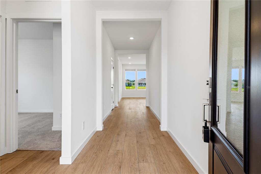 A bright entryway features light wood-look flooring, white walls, and a view toward a window — 5550 GUAVA COURT, KISSIMMEE, FL