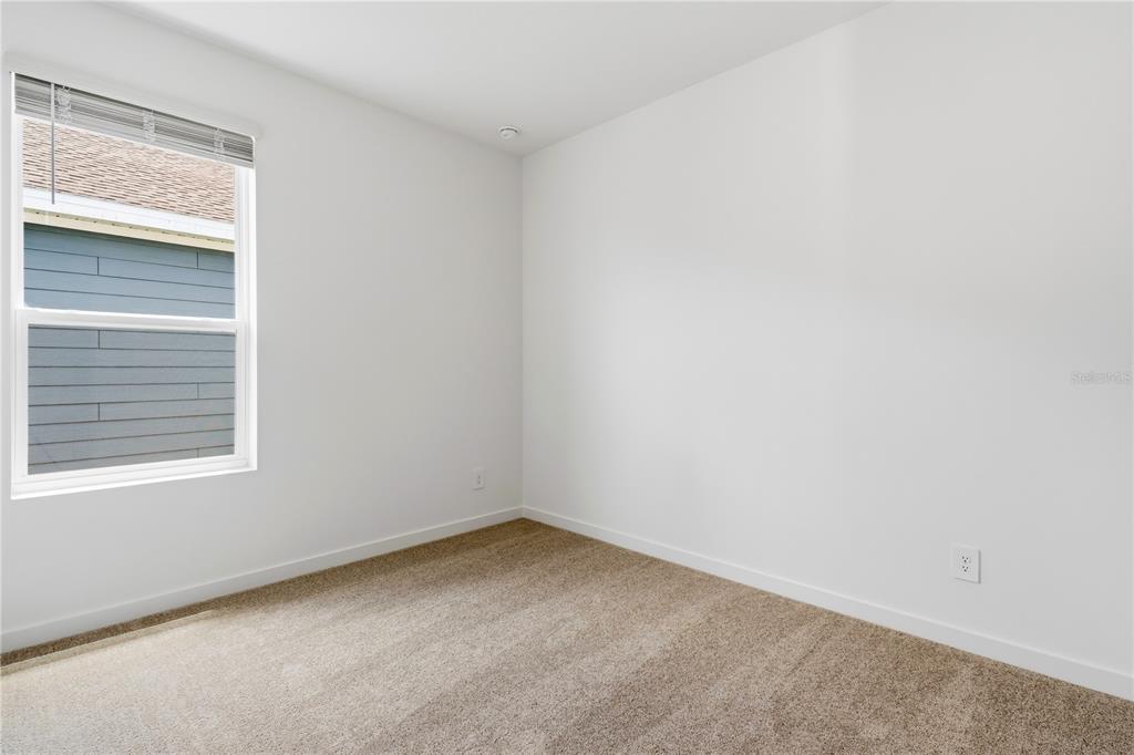 An empty bedroom features white walls, tan carpet, and a single window with blinds — 5550 GUAVA COURT, KISSIMMEE, FL