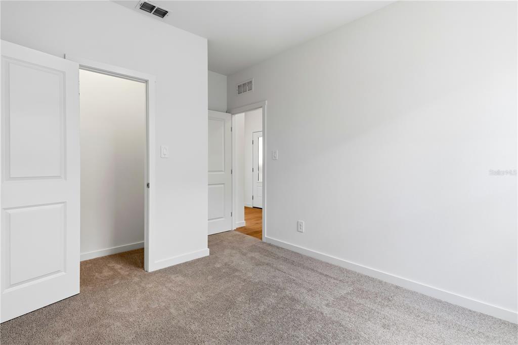 An empty bedroom with gray carpet, white walls, and two open doorways — 5550 GUAVA COURT, KISSIMMEE, FL