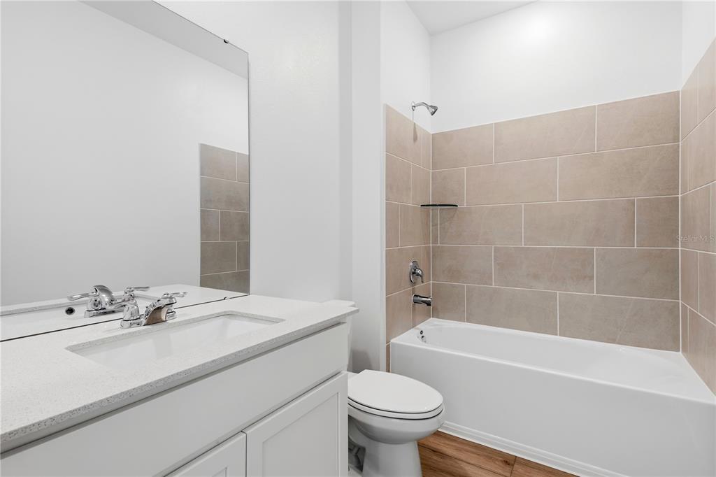 A bathroom features a white vanity, a toilet, and a bathtub with beige tiled walls — 5550 GUAVA COURT, KISSIMMEE, FL