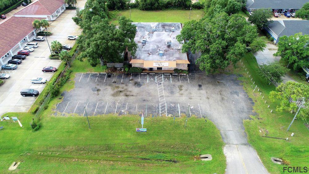 An aerial view shows a commercial building with a large parking lot and surrounding trees — 4701 E MOODY BOULEVARD, BUNNELL, FL