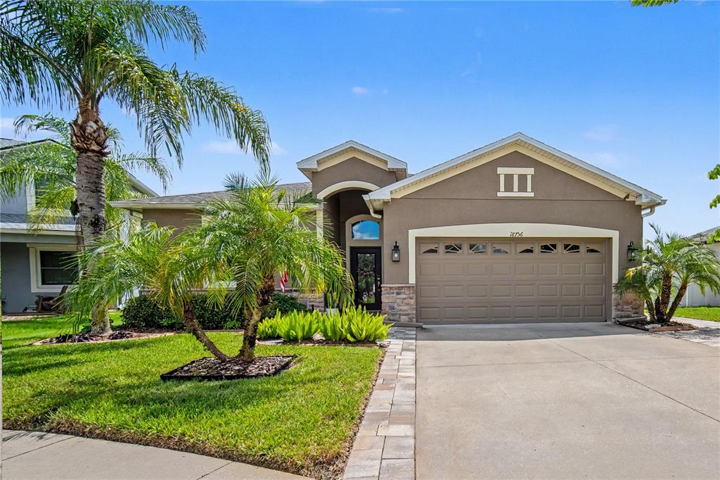 A single-story house with a tan stucco exterior, a two-car garage, and palm trees — 18756 BURNDALL COURT, LAND O LAKES, FL