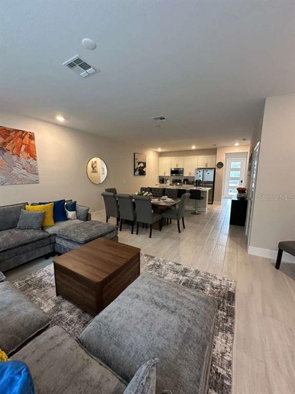 An open-concept living room and kitchen feature gray tile flooring and neutral walls — 7789 SPECTRUM DRIVE, REUNION, FL