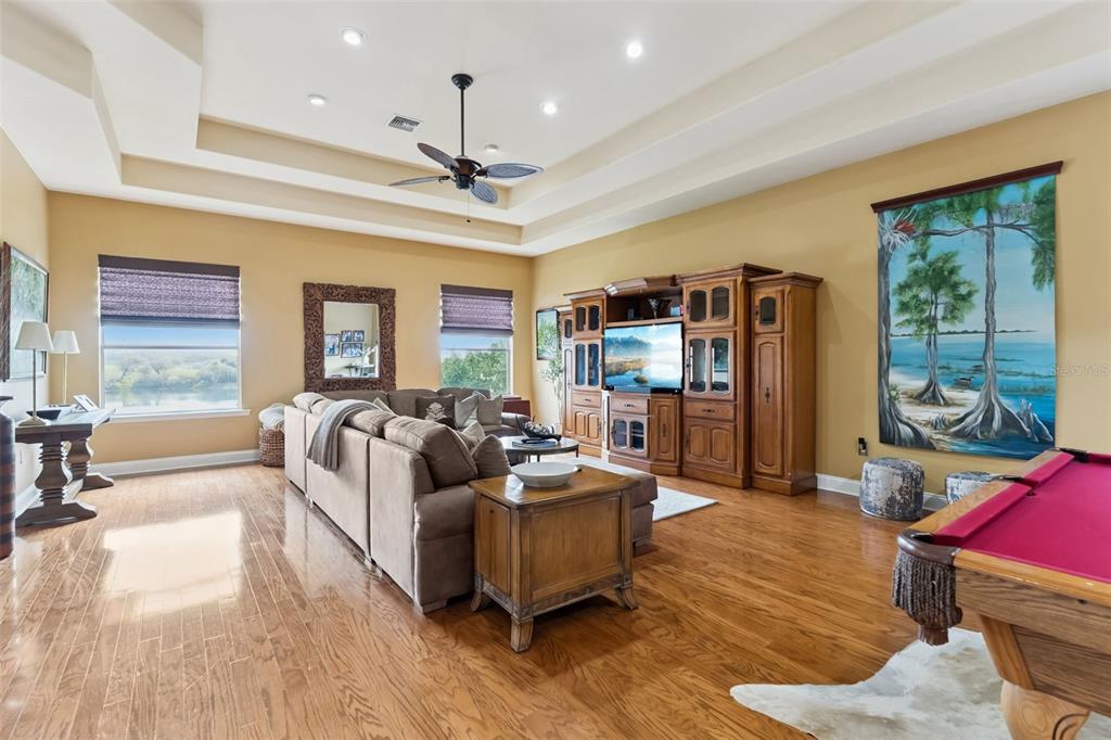 A spacious living room features hardwood floors, a tray ceiling, a sectional sofa, and a pool table — 3231 HARBOR BEACH DRIVE, LAKE WALES, FL