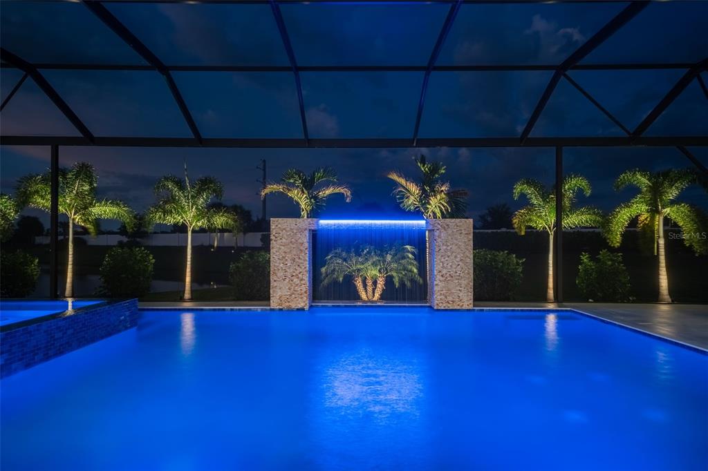 A swimming pool at night features a stone water feature with blue LED lighting — 8207 NEVIS RUN, LAKEWOOD RANCH, FL