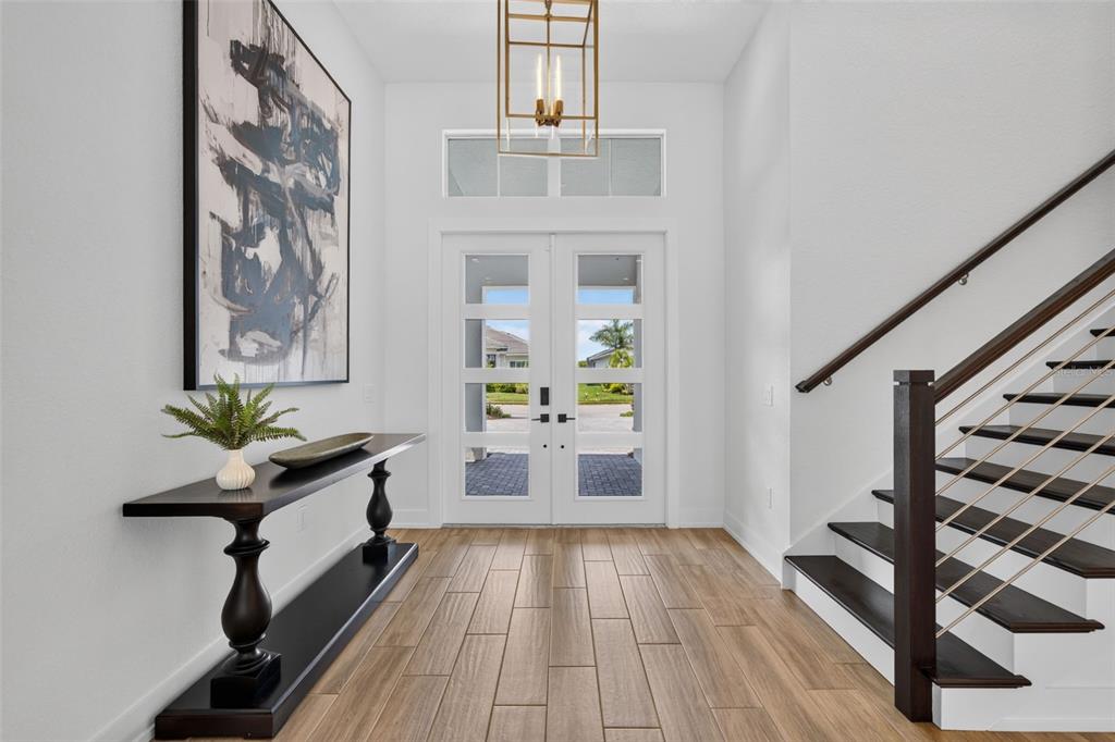 A bright foyer features wood-look tile flooring, a dark console table, and a modern staircase — 8207 NEVIS RUN, LAKEWOOD RANCH, FL