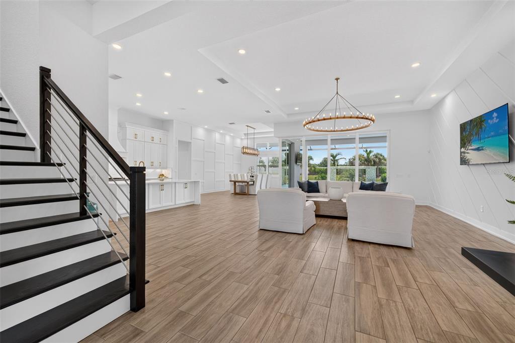An open-concept living room and kitchen featuring wood-look tile flooring and a modern staircase — 8207 NEVIS RUN, LAKEWOOD RANCH, FL