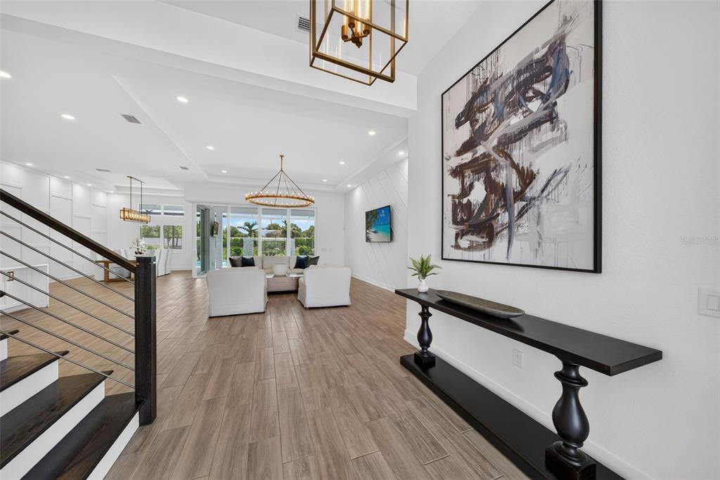 A bright, open-concept living area features wood-look tile flooring, a modern chandelier, and a console table — 8207 NEVIS RUN, LAKEWOOD RANCH, FL
