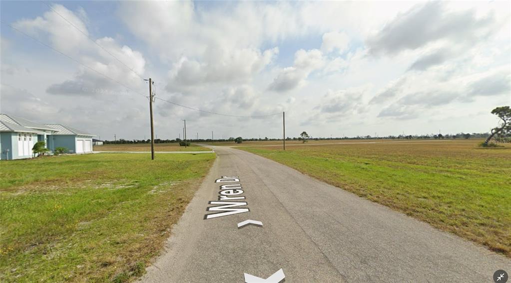 A paved road leads through a flat, grassy landscape with a house on the left — 96 WREN DRIVE, PLACIDA, FL