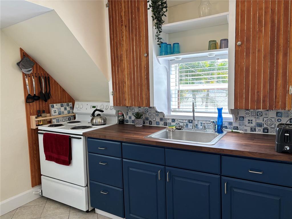 A kitchen features blue lower cabinets, wood-paneled upper cabinets, a white stove, and patterned backsplash tiles — 810 22ND AVENUE N UNIT 2, ST PETERSBURG, FL