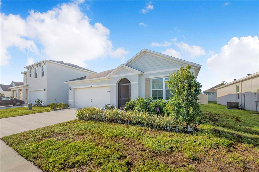 A light blue single-story house with a two-car garage and a landscaped front yard — 1704 FROGMORE AVENUE, HAINES CITY, FL
