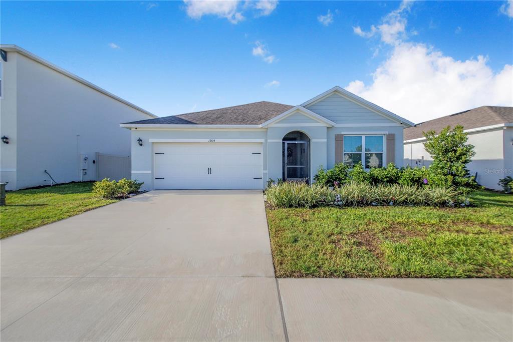 A single-story suburban house with a two-car garage, light blue siding, and a concrete driveway — 1704 FROGMORE AVENUE, HAINES CITY, FL