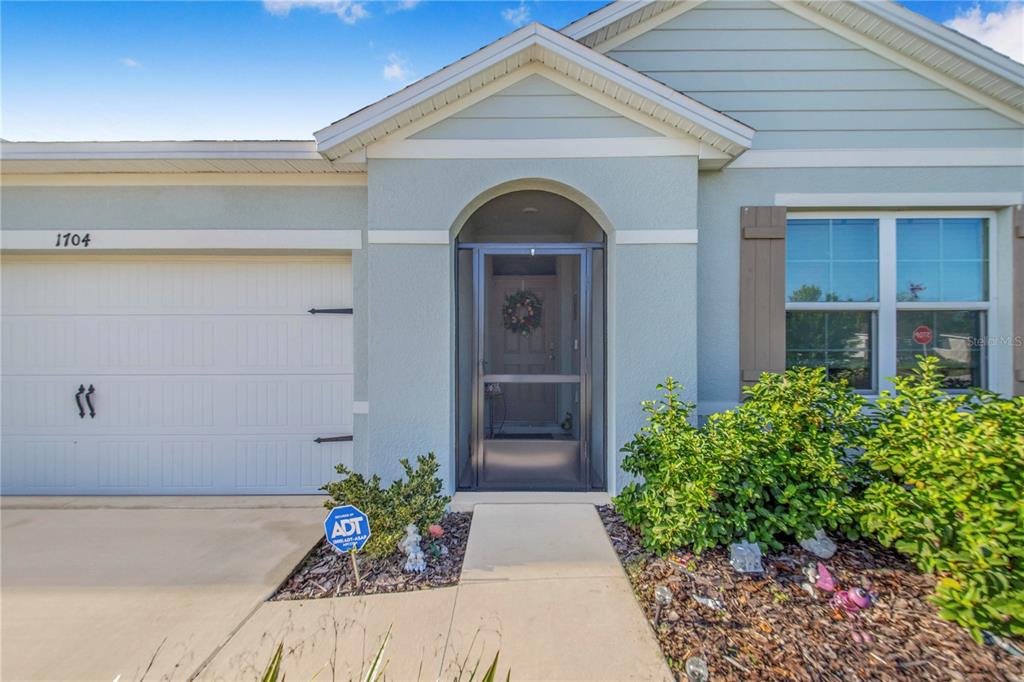 The exterior of a house features a garage, a front entrance with a screen door, and landscaping — 1704 FROGMORE AVENUE, HAINES CITY, FL