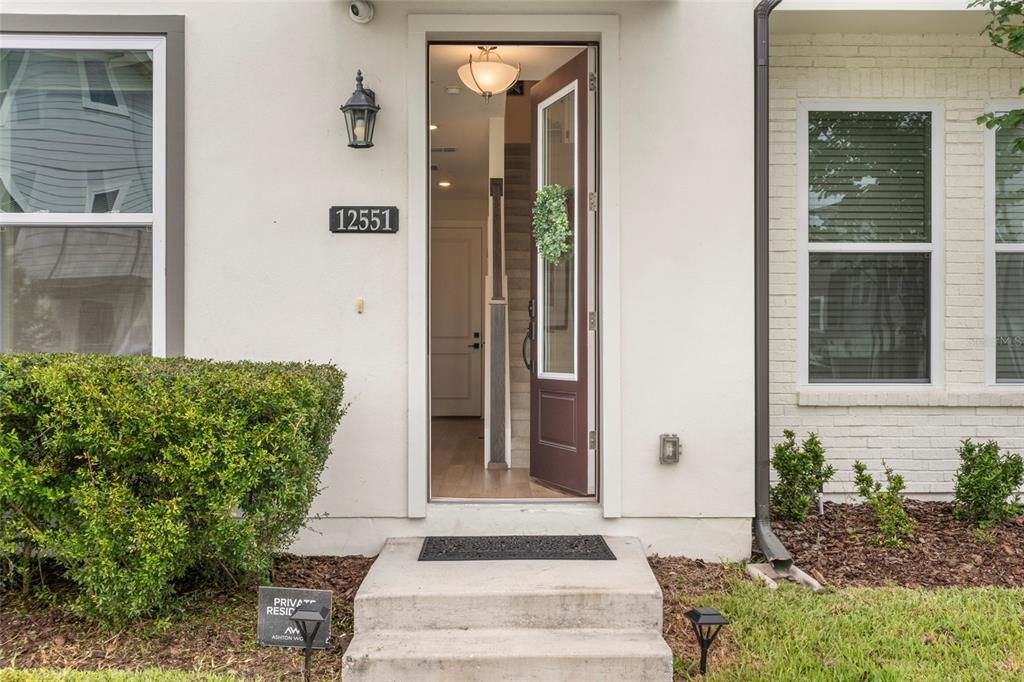 A multi-story townhouse with white siding and dark trim sits along a sidewalk — 12551 WILLSTATTER AVENUE, ORLANDO, FL