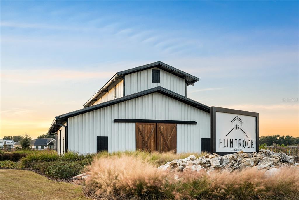 A white barn-style building with dark trim stands behind a sign labeled Flintrock Agrihood — Lot 46 SW 125TH CIRCLE, ARCHER, FL