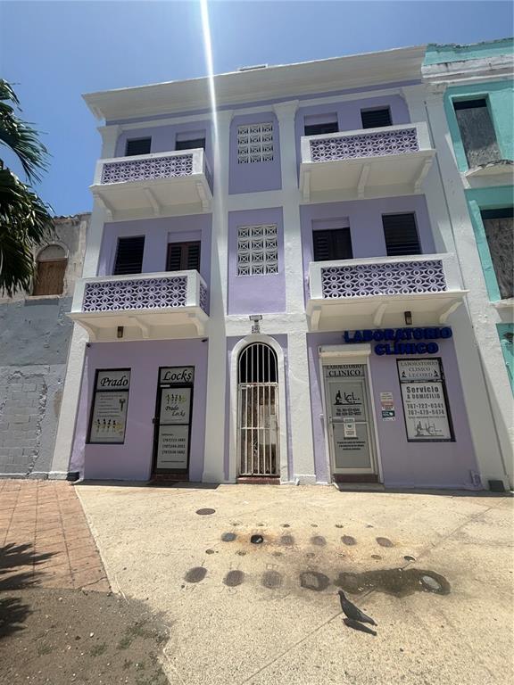 A three-story lavender building features two ground-level storefronts, decorative balconies, and a central arched entrance — 260 CONSTITUCION, SAN JUAN, PR
