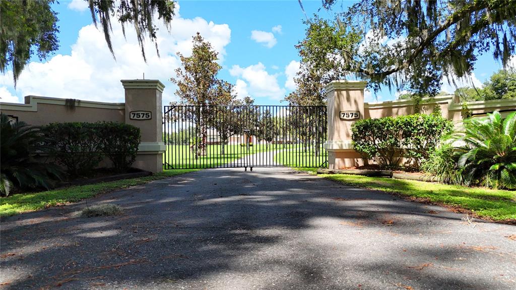 A gated entrance features a paved driveway leading to a metal gate between two pillars — 7571 W HIGHWAY 326, OCALA, FL